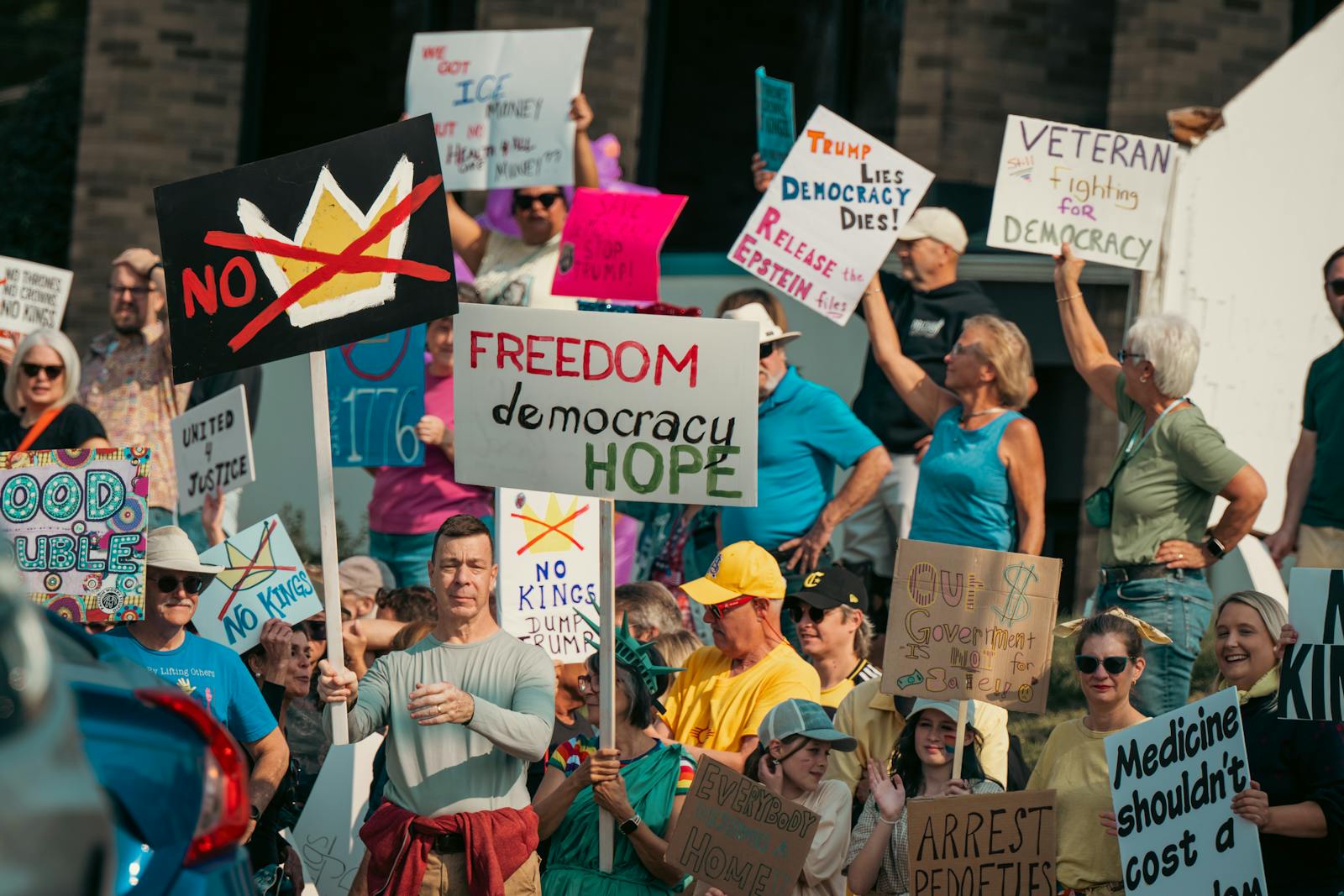 Pro-democracy demonstrators holding handmade signs that say freedom, democracy, hope, and no kings.